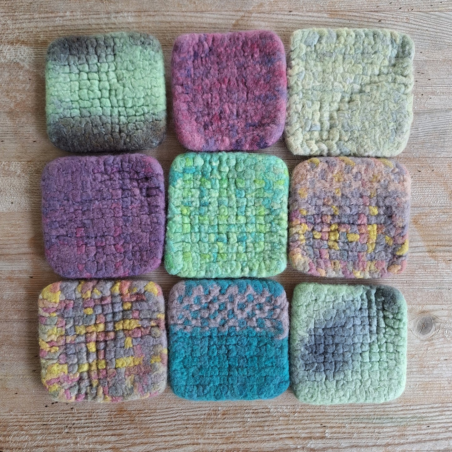 Nine felted wool coasters in various colors on a wooden surface