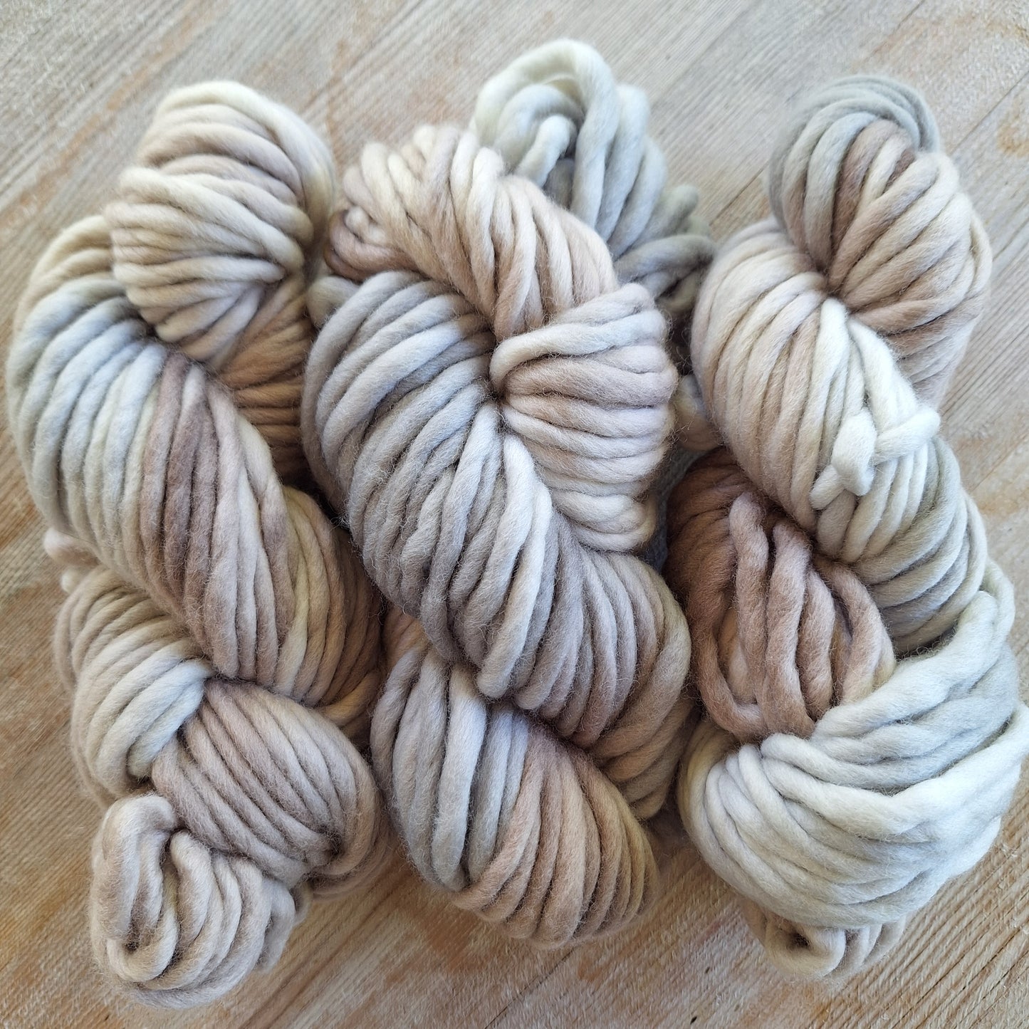 Three skeins of cream and beige pencil roving yarn on a wooden surface