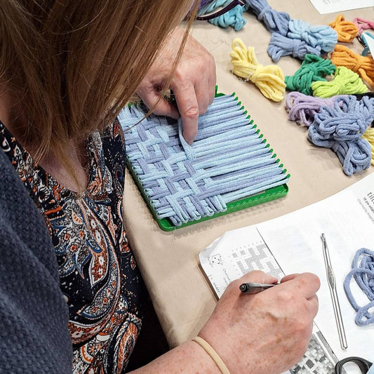 Student working on a potholder weaving with colorful loops and a pattern book.