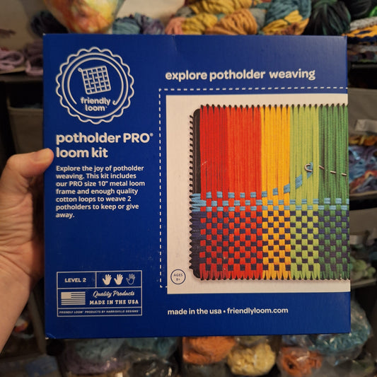 Blue box of a potholder loom kit held by a hand with colorful yarn in the background.