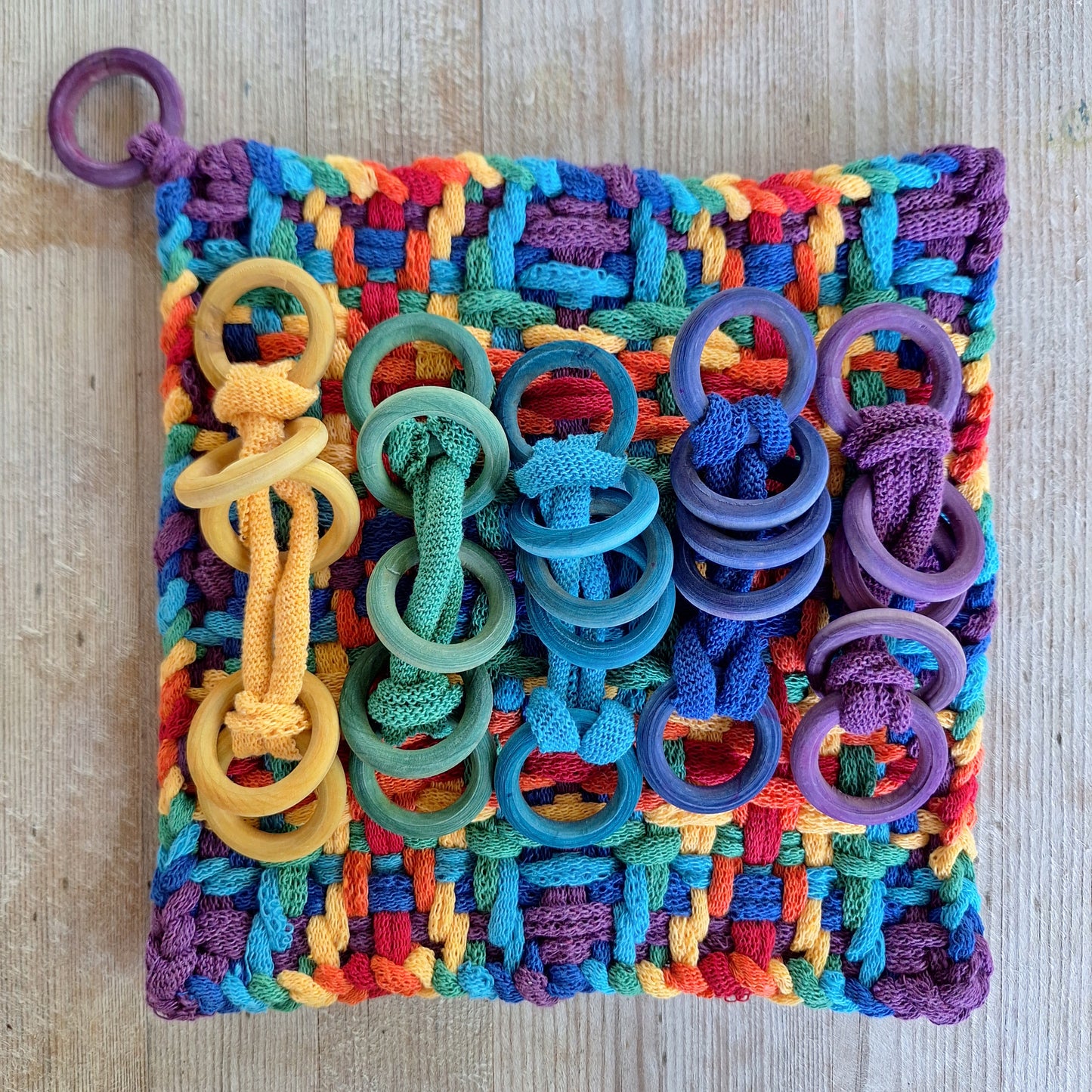 Colorful woven potholder with hand dyed wooden rings on a wooden surface