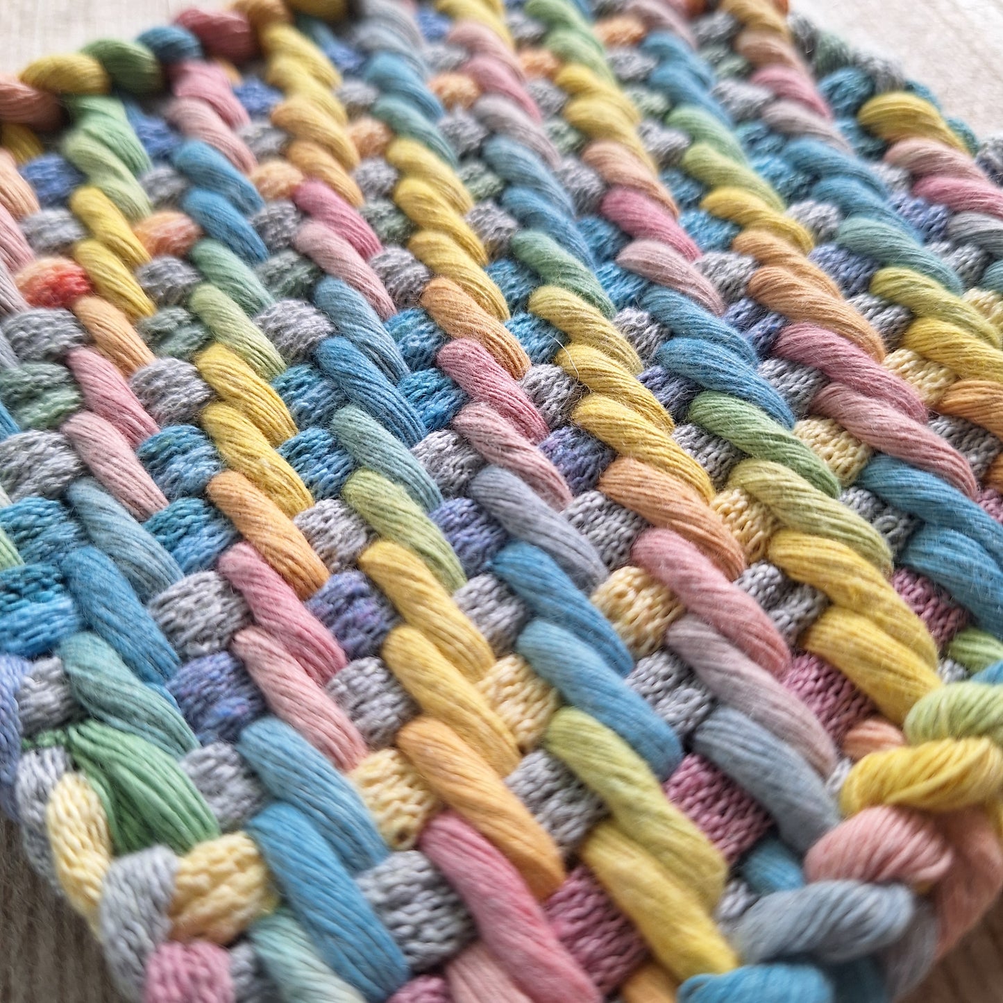 Close-up of a multicolored woven trivet with pastel shades of cotton cord and potholder loops.