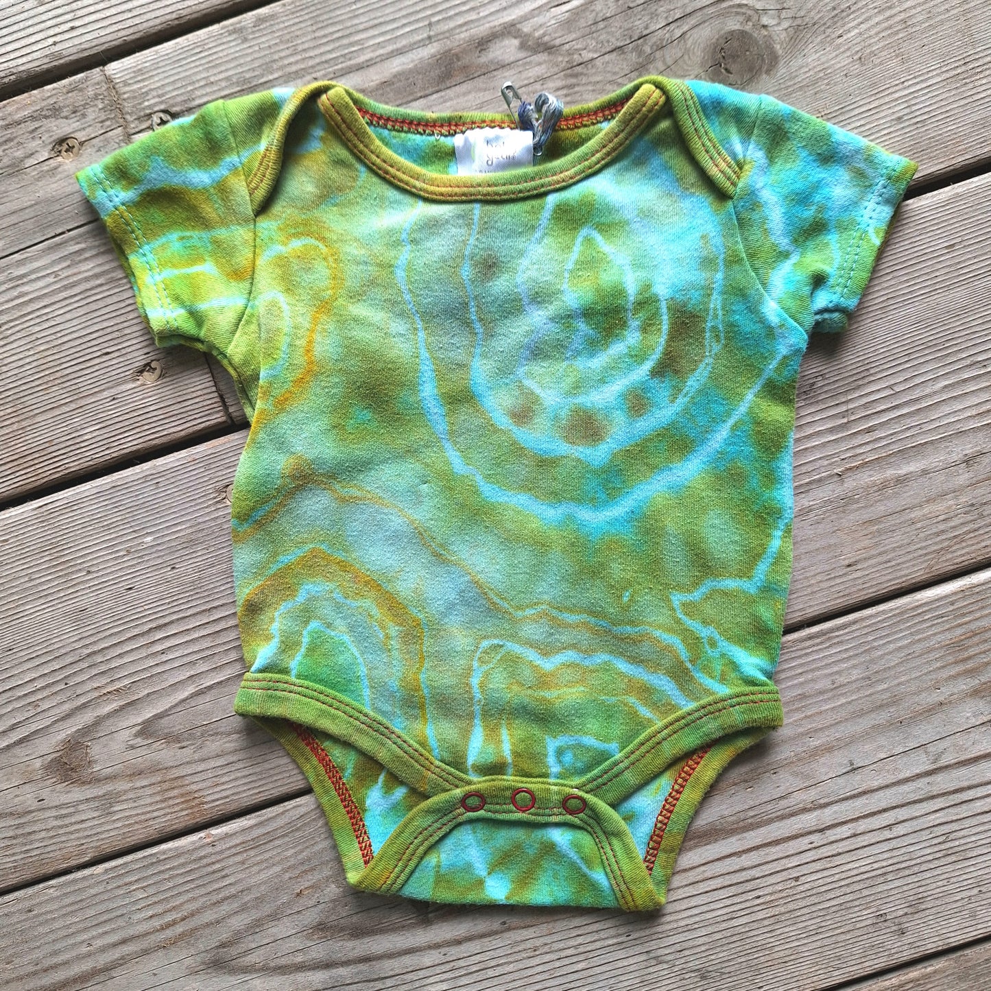 Green and blue tie-dye baby onesie on a wooden surface
