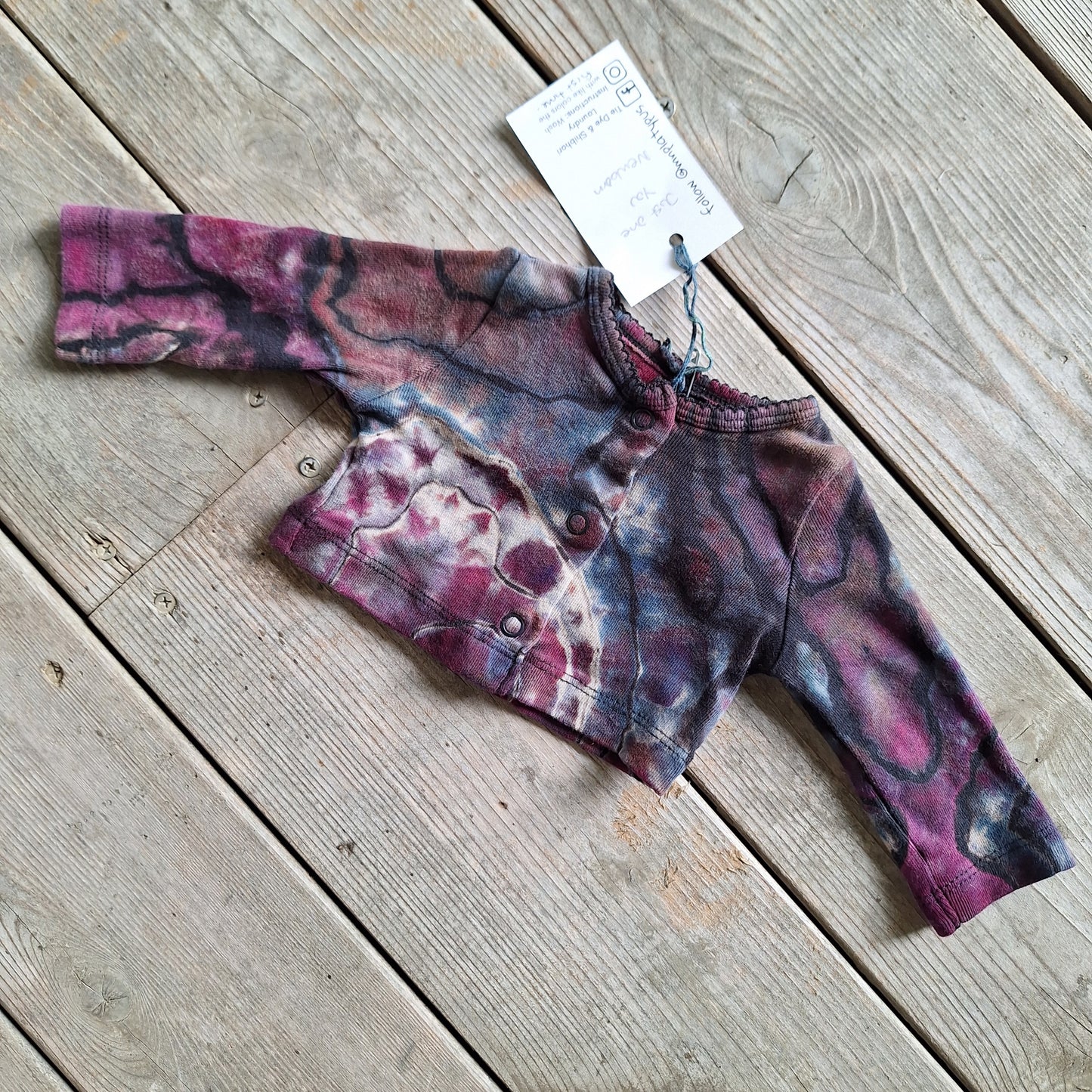 Purple tie-dye baby sweater on a wooden surface with a tag attached.