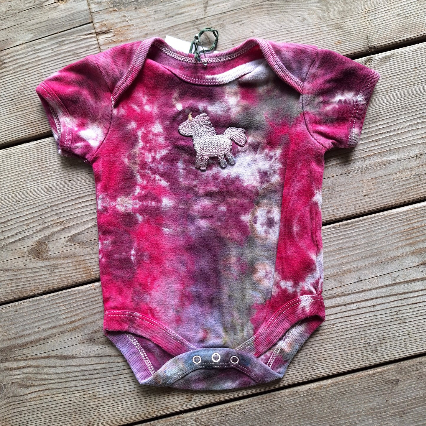 Pink tie-dye baby onesie with a unicorn patch on a wooden surface