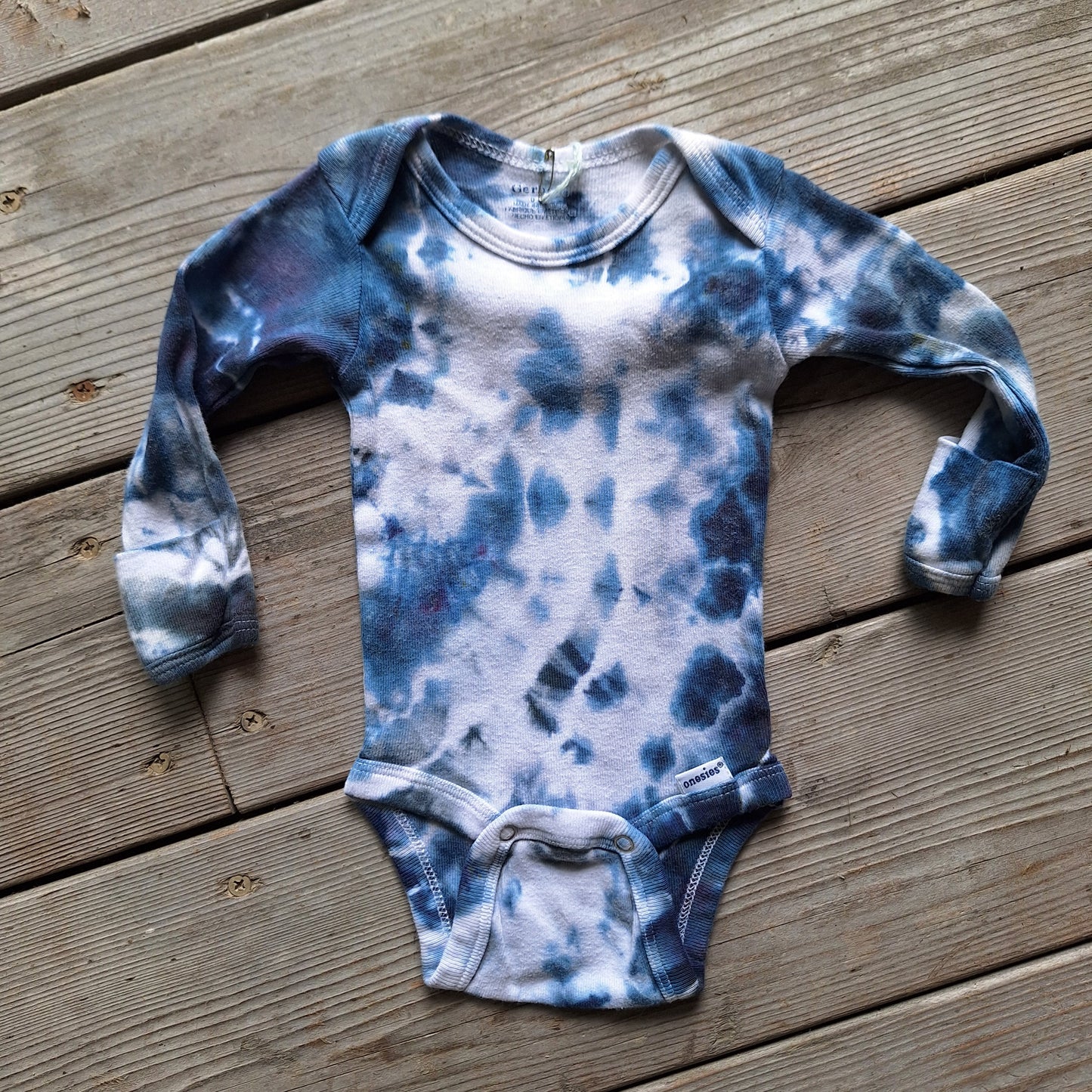 Blue and white tie-dye baby onesie on a wooden surface