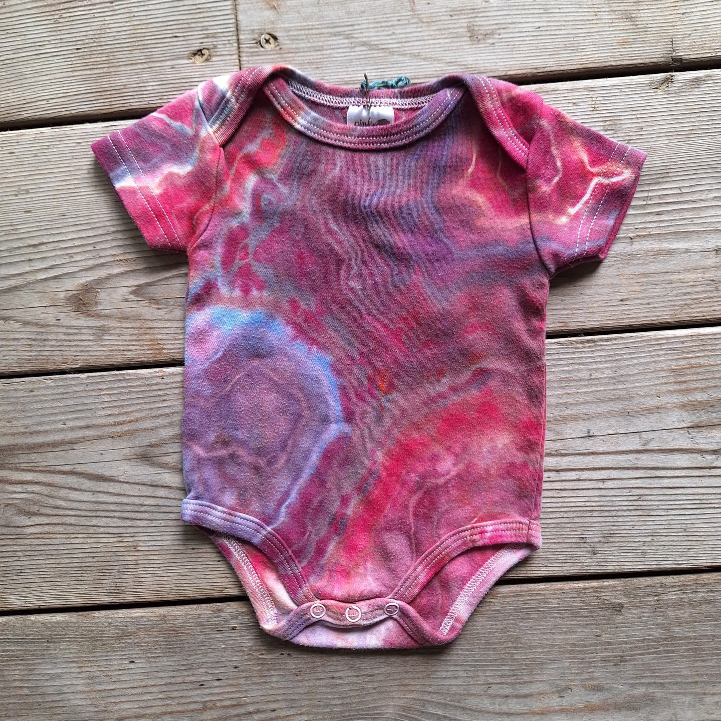 Pink and purple tie-dye baby onesie on a wooden surface