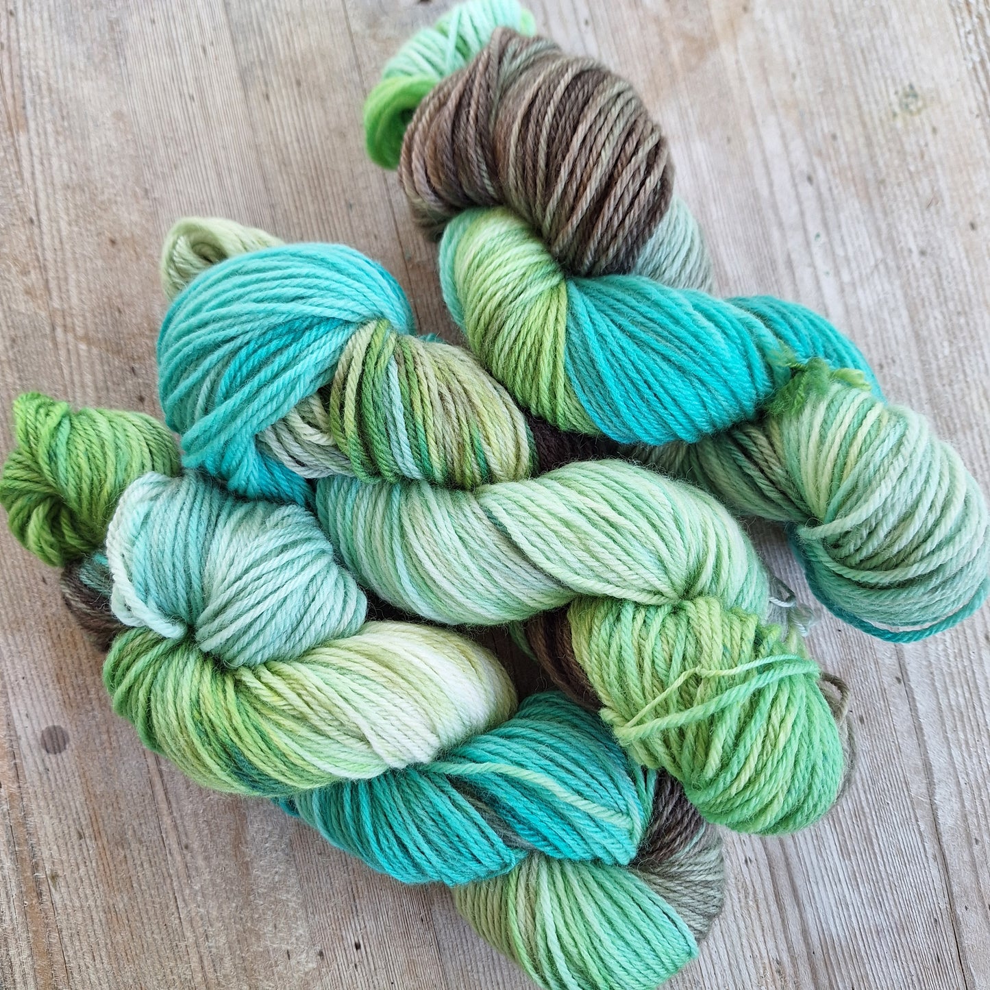 Green and brown yarn skeins on a wooden surface