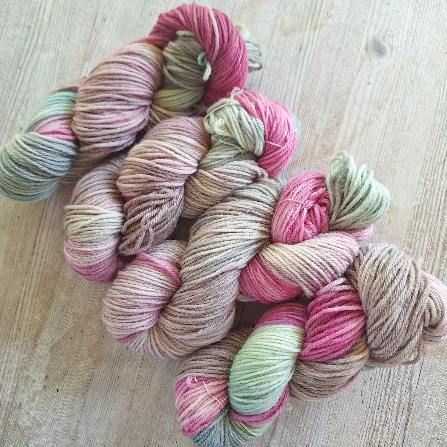 Pink and green worsted weight wool yarn skeins on a wooden surface