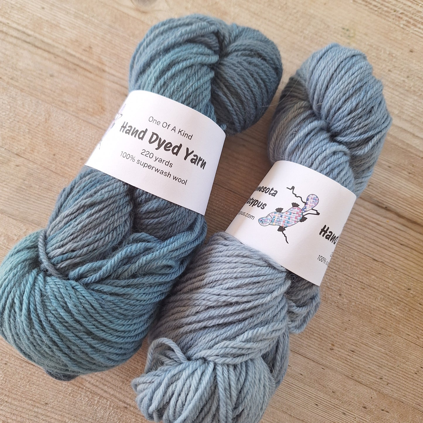 Two skeins of blue yarn with labels on a wooden surface