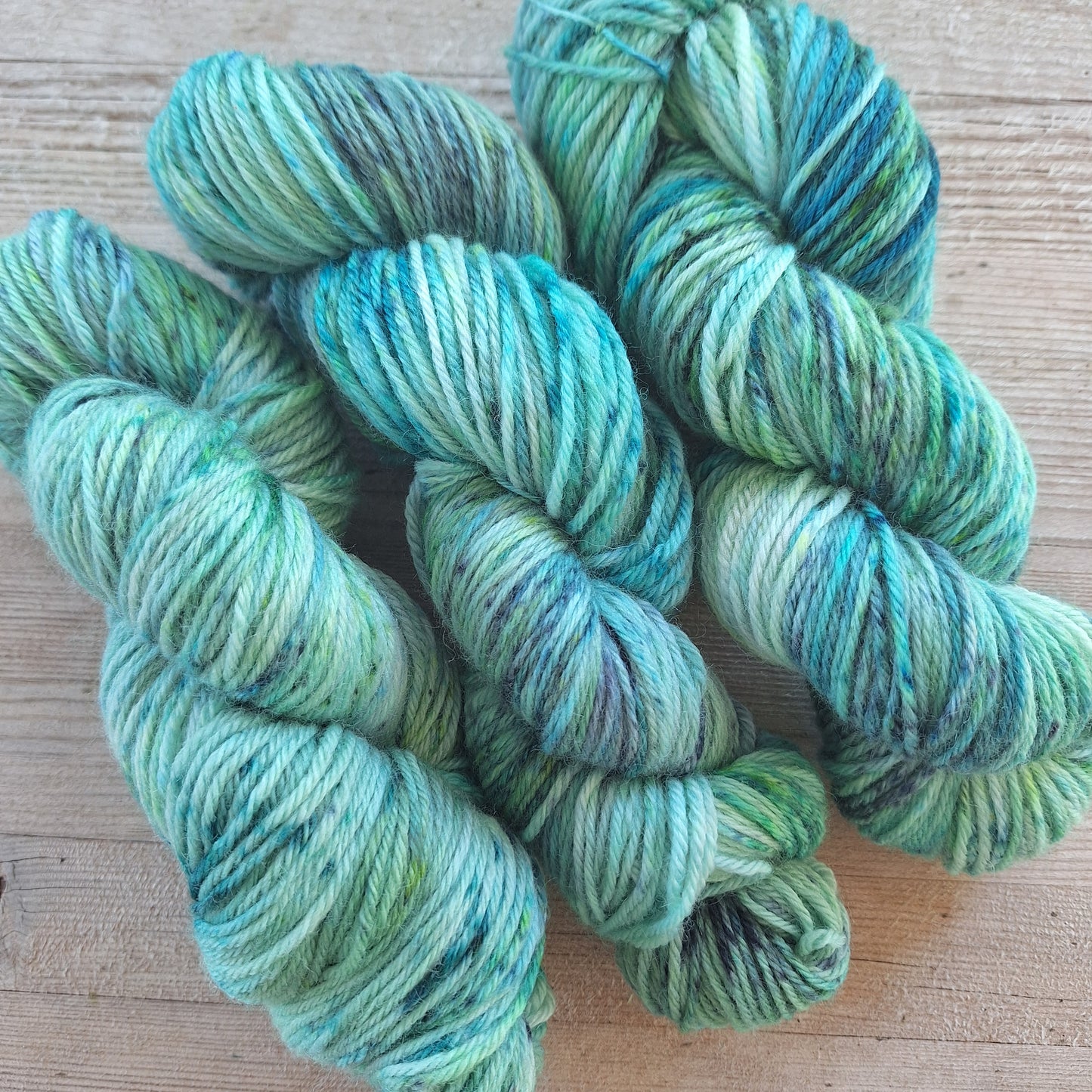 Three skeins of speckled green and blue yarn on a wooden surface