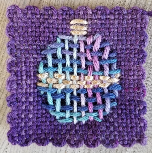 Embroidered design on a purple woven square with a christmas ornament shape.