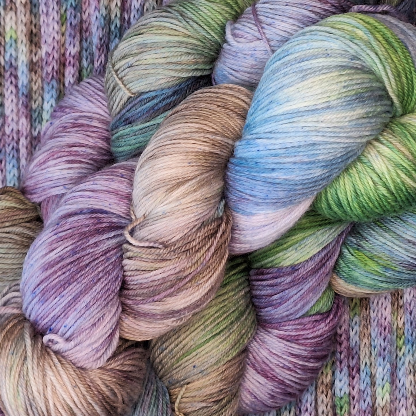 Close-up of colorful yarn skeins in various shades of green, purple, and brown on an i-cord background