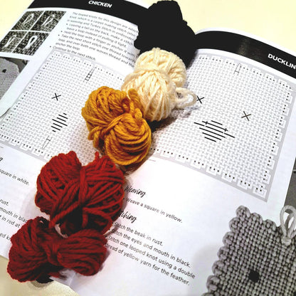 Yarn balls laying on an open weaving pattern booklet showing chicken and duckling pages