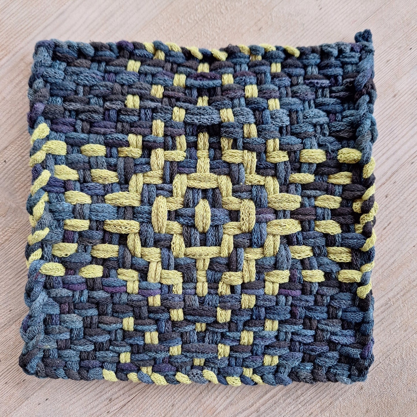 Woven potholder with blue and green pattern on a wooden surface