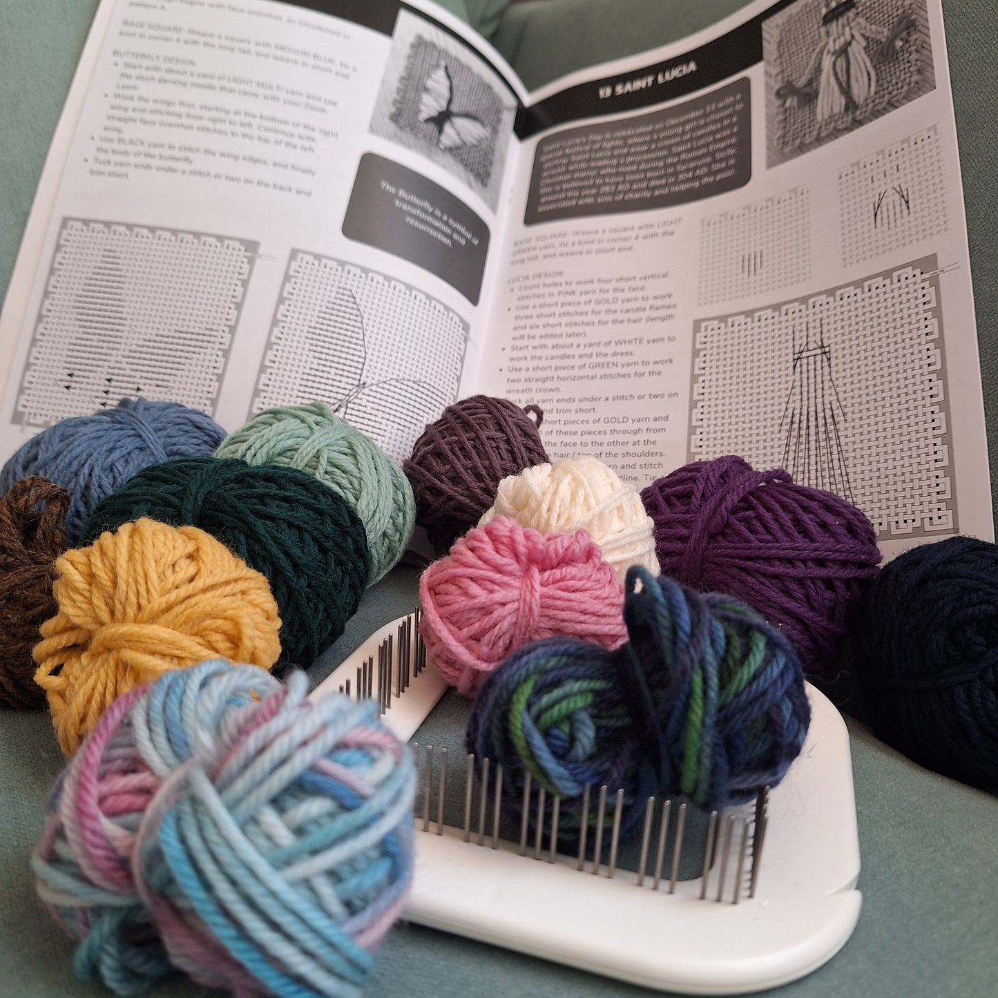 Colorful yarn balls and a Zoom Loom laying on an open pattern book showing butterfly and Saint Lucia patterns