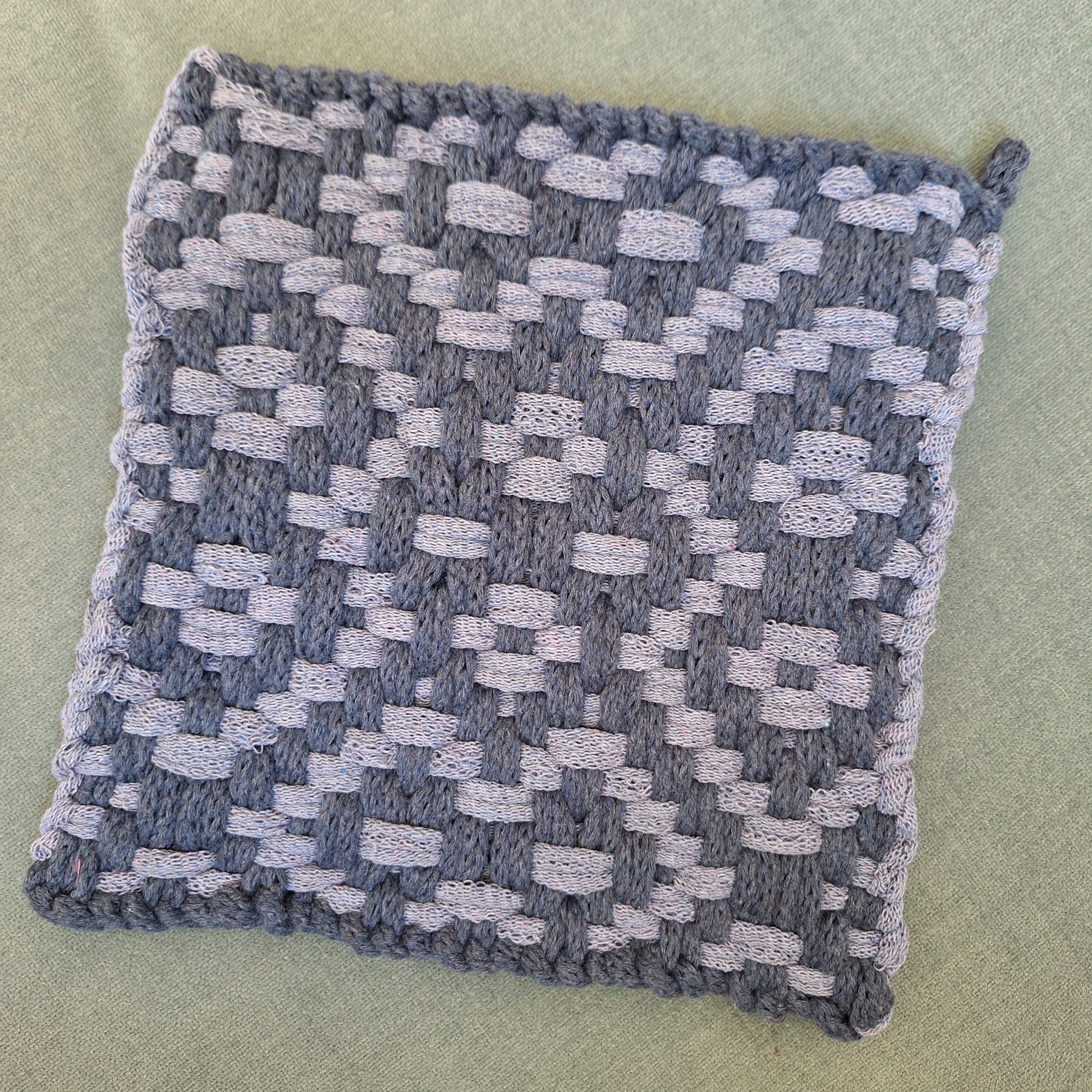 Textured blue and gray patterned pot holder on a muted green background