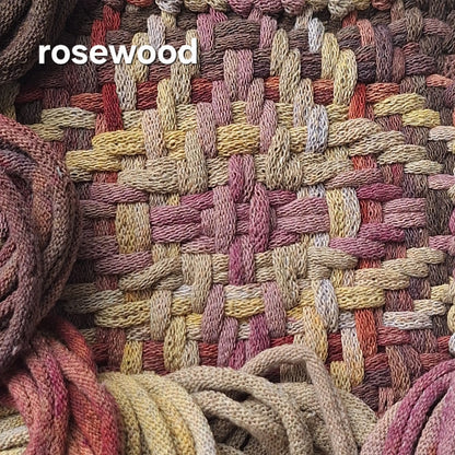 Close-up of a woven potholder in a variegated rosewood color palette, featuring interwoven strands of dusty pink, mauve, beige, brown, and muted red. The word 'rosewood' is printed in white text in the upper left corner.