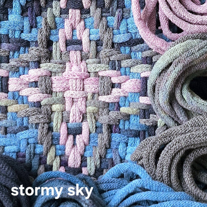 Close-up of woven trivet with blue and warm grey loops and 'stormy sky' text.