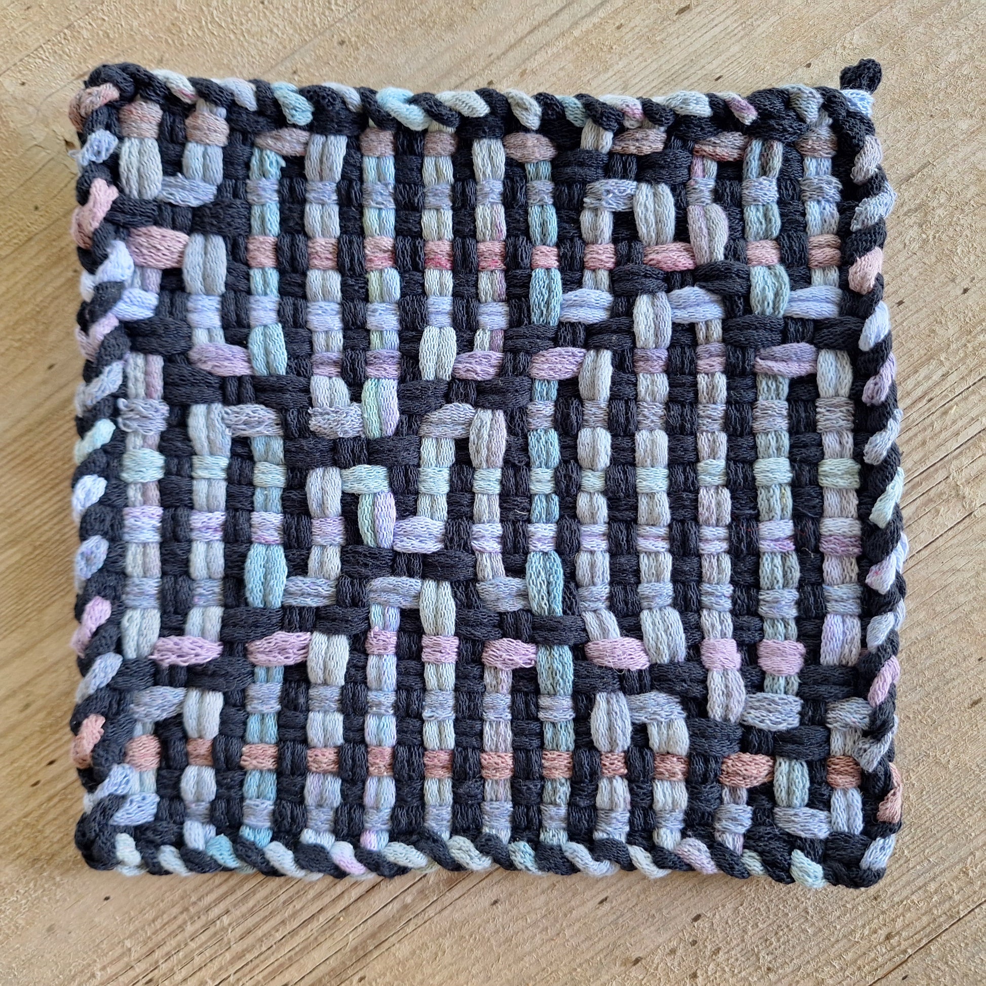 Woven potholder with multicolor city skyline pattern on a wooden surface
