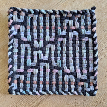 Woven potholder with multicolor city skyline pattern on a wooden surface