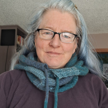 Person with gray hair and glasses wearing a blue woven cowl scarf with drawstrings indoors.