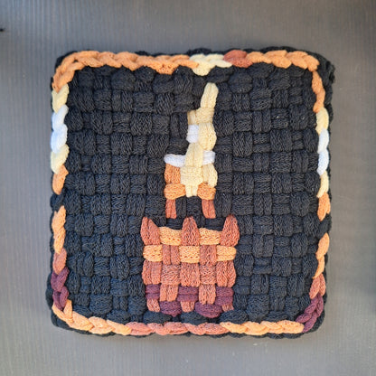 Woven potholder with a candle image and multicolored border on a gray background