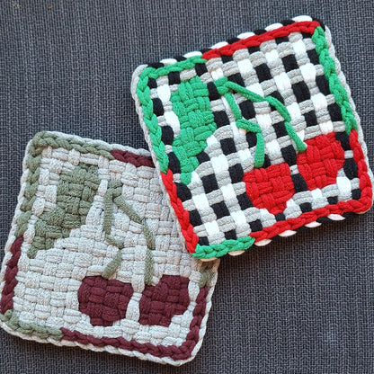 Two woven trivets with cherry patterns on a gray surface
