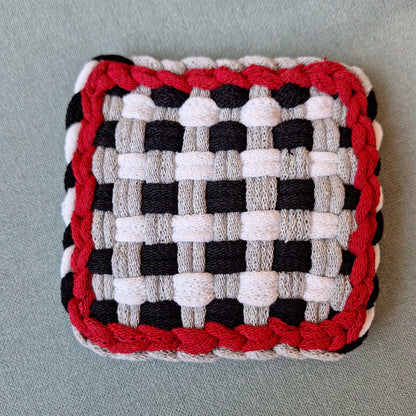 Woven square trivet with red, black, and white gingham pattern on a gray background