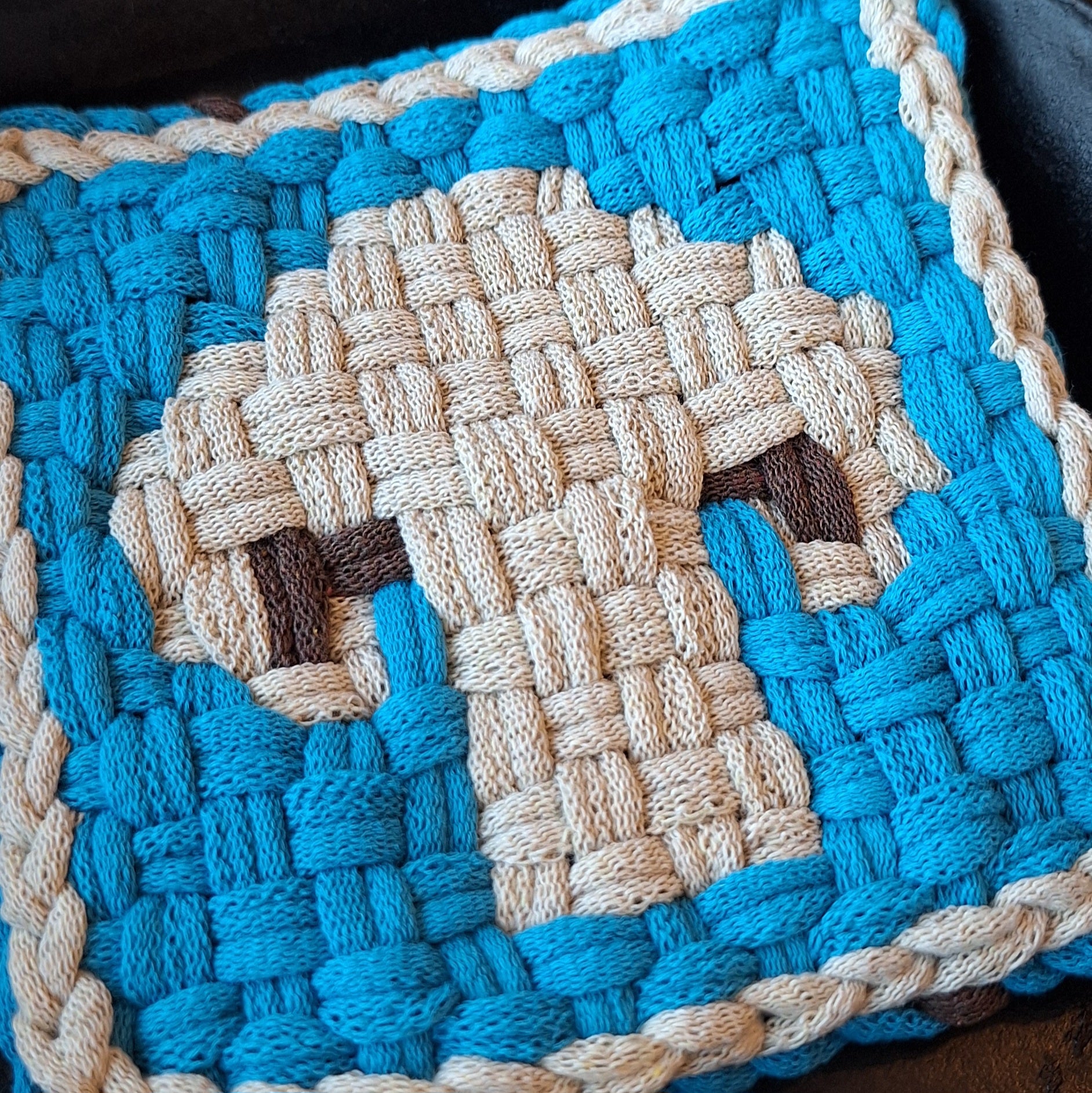 Close-up of a woven blue and beige trivet with a mushroom pattern.