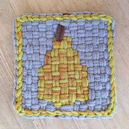 Woven potholder with a pear pattern on a wooden surface