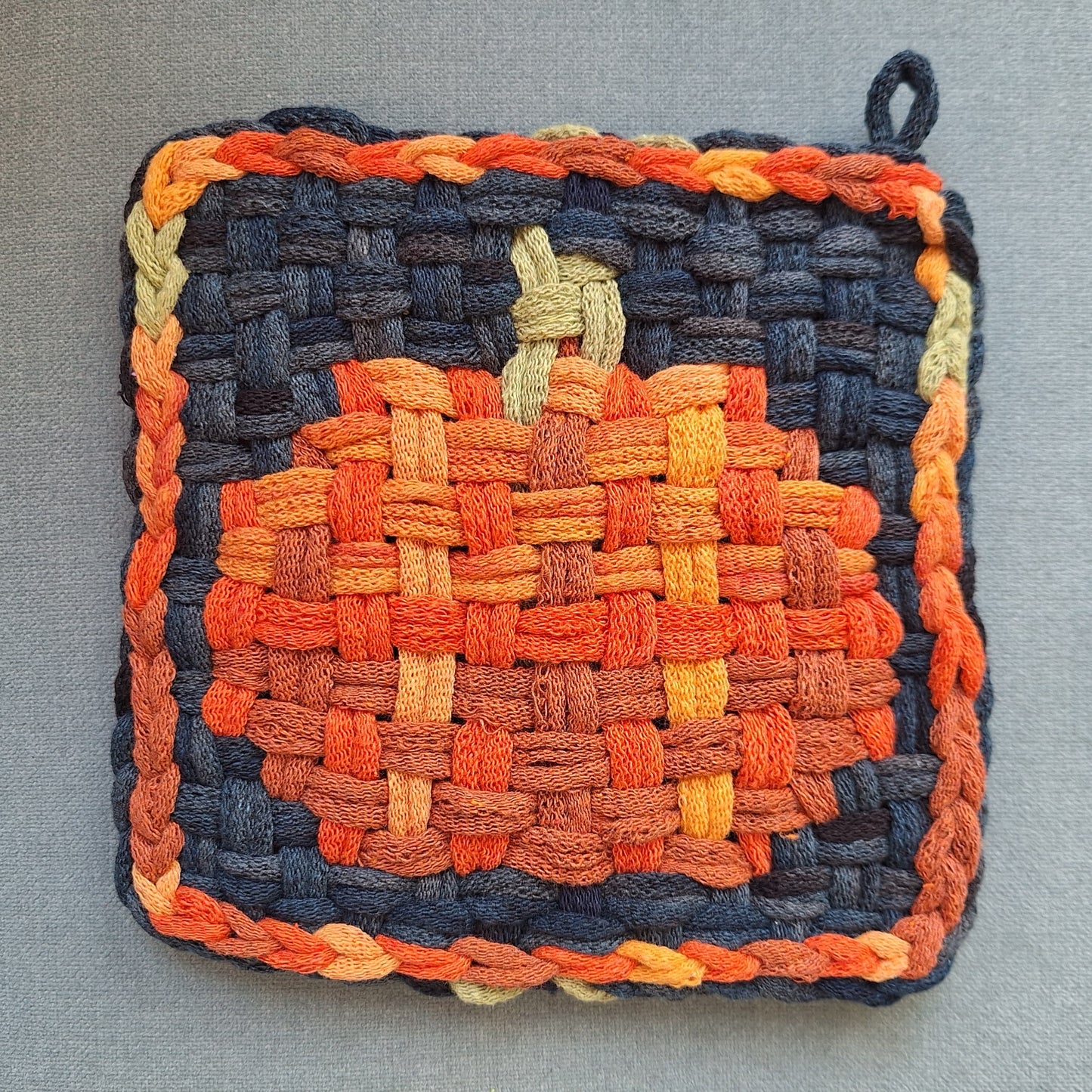 Woven potholder with pumpkin design on a gray background