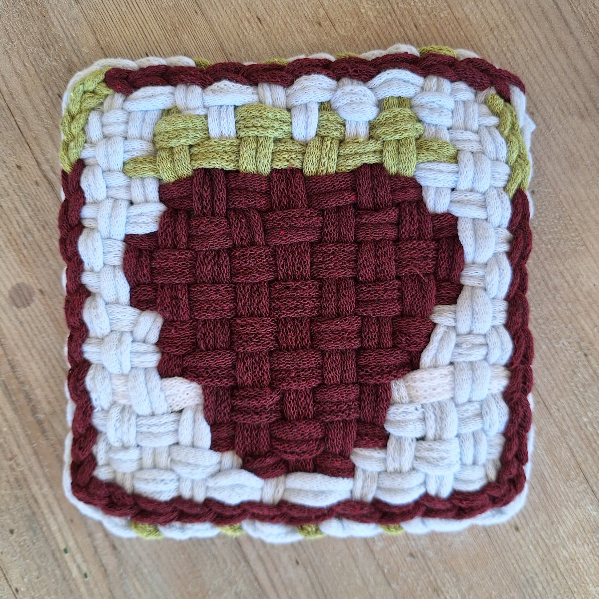 Woven square trivet with a raspberry pattern on a wooden surface