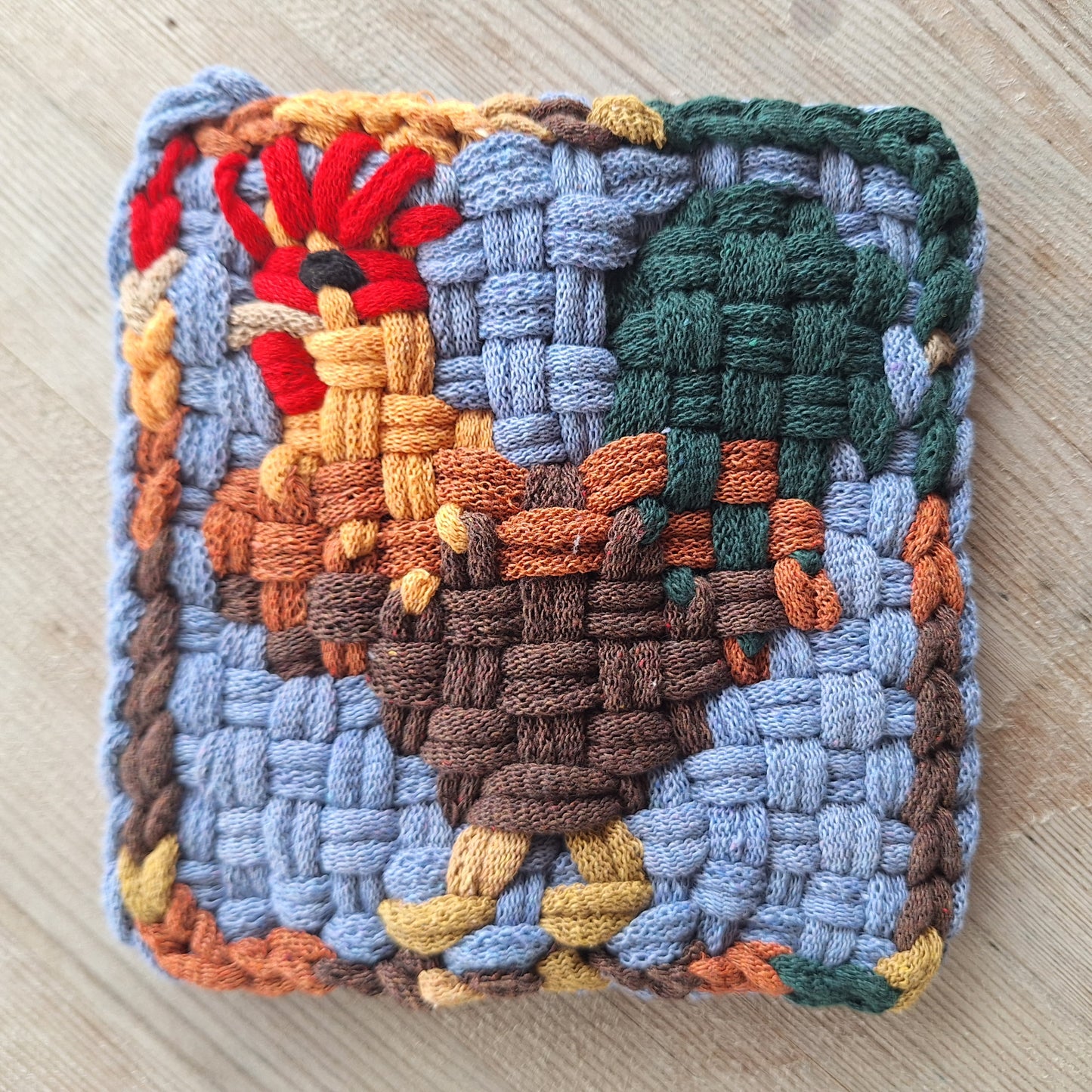 Woven trivet with a rooster design on a wooden surface