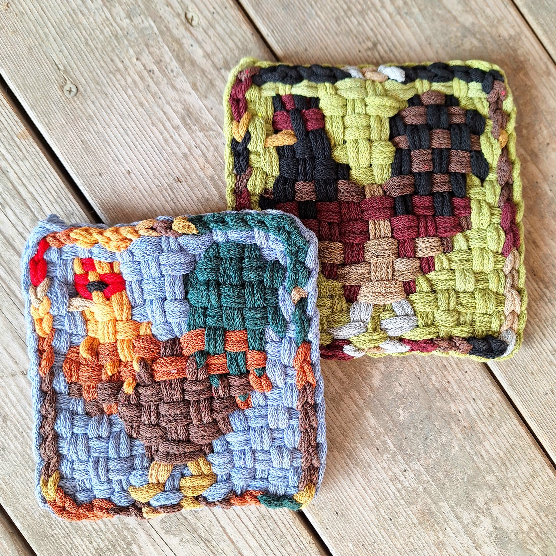 Two woven potholders with geometric rooster patterns on a wooden surface