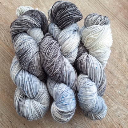 Three skeins of gray and white yarn on a wooden surface