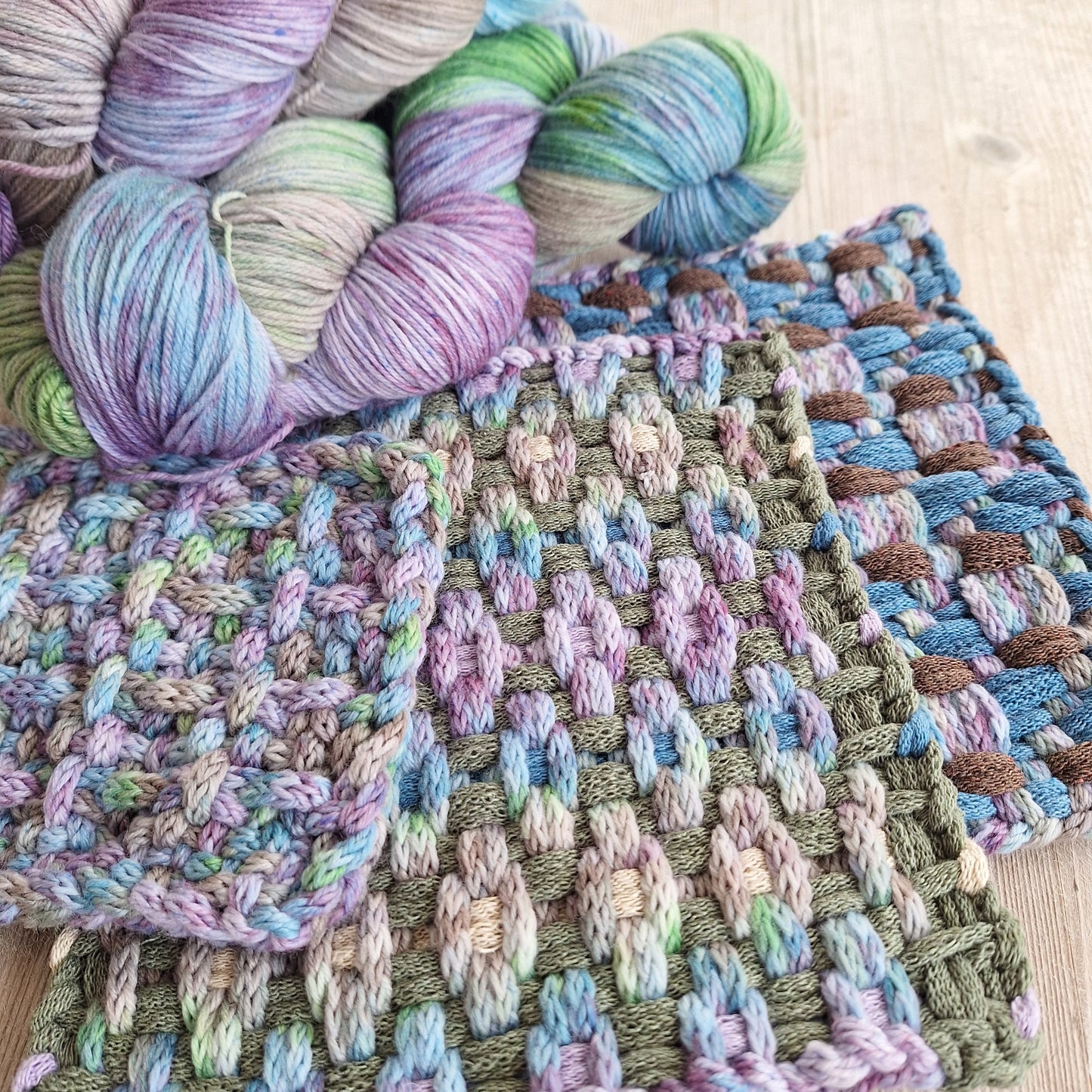 Colorful potholders woven with icord next to yarn skeins on a wooden surface