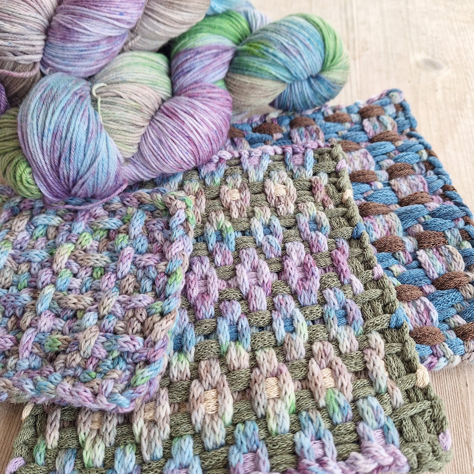 Colorful potholders woven with icord next to yarn skeins on a wooden surface