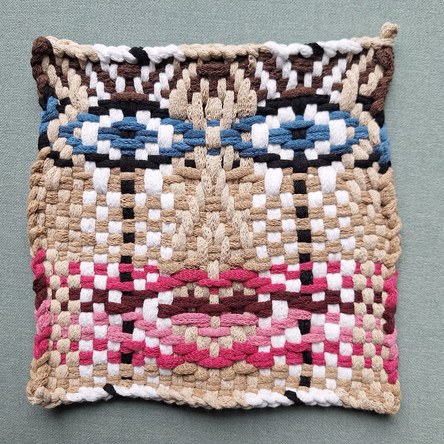 Woven potholder with geometric face pattern on a gray background
