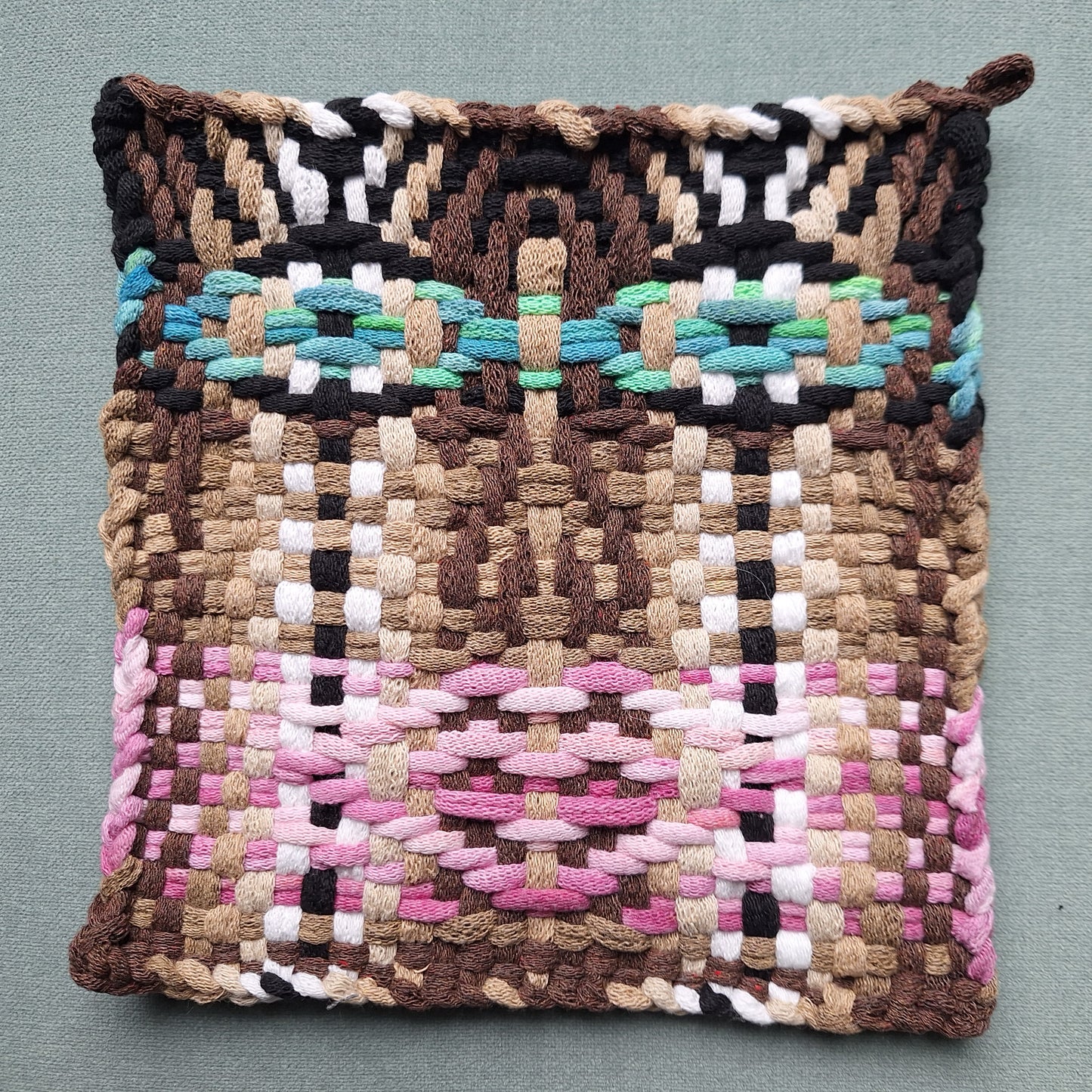 Woven potholder with multicolored face pattern on a gray background