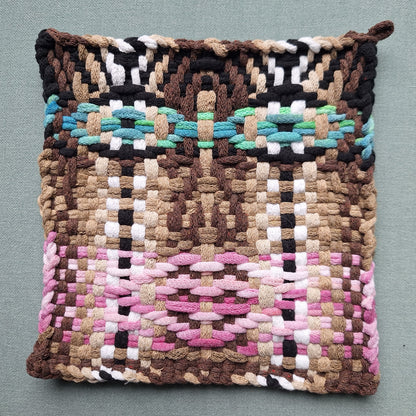 Woven potholder with multicolored face pattern on a gray background