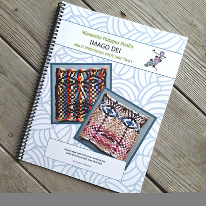 A spiral-bound book titled 'Minnesota Platypus Studio IMAGO DEI' lies on a weathered wooden surface. The cover features a white background with a light blue wave pattern, two colorful woven textile examples, and text describing a multi-directional split loop twill.