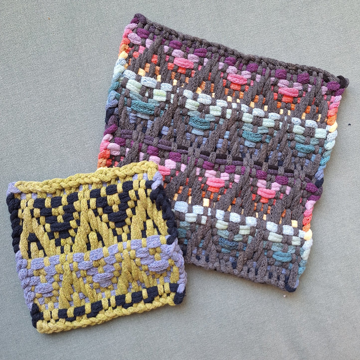 Two woven potholders with colorful patterns on a gray surface