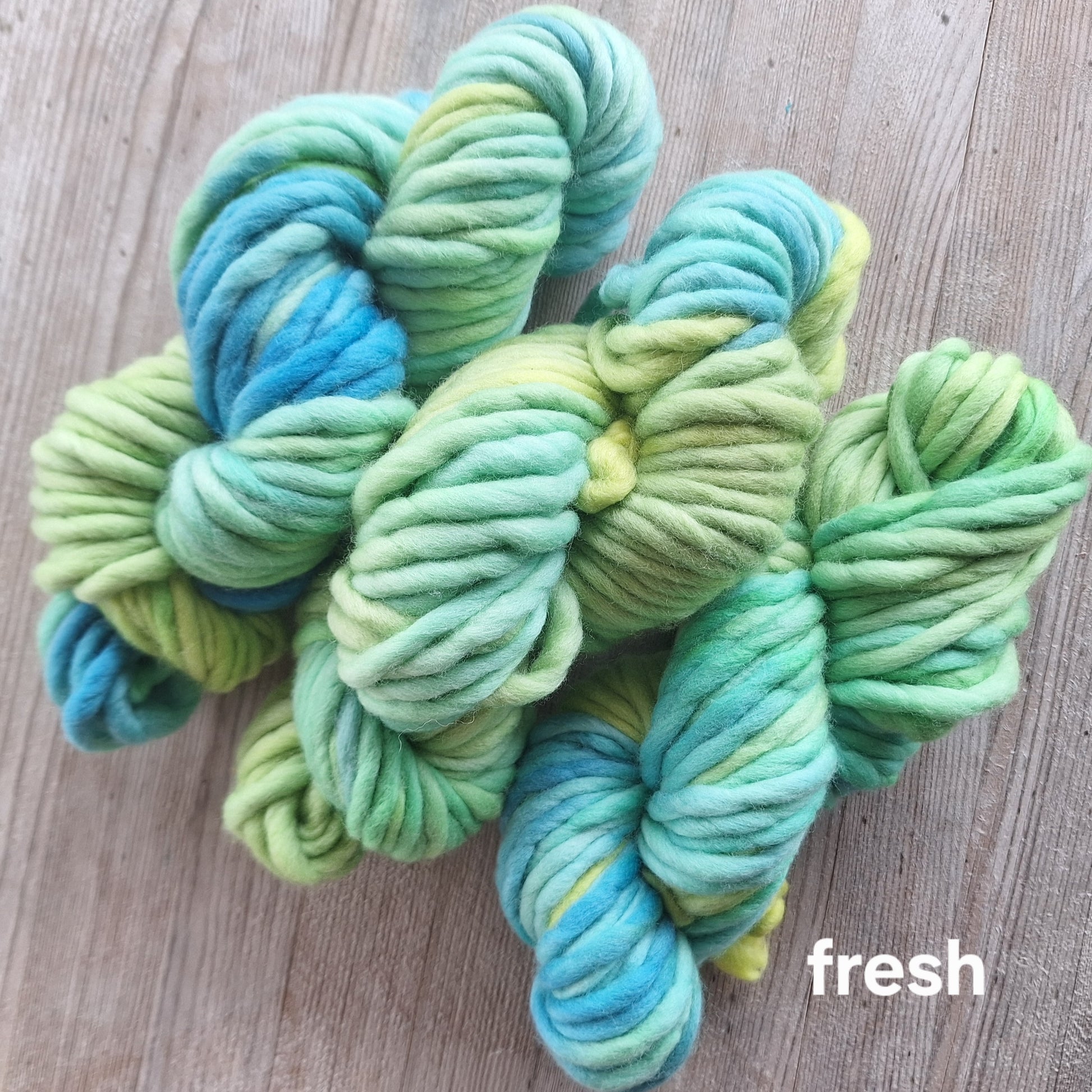 Green and blue yarn skeins on a wooden surface with 'fresh' text.