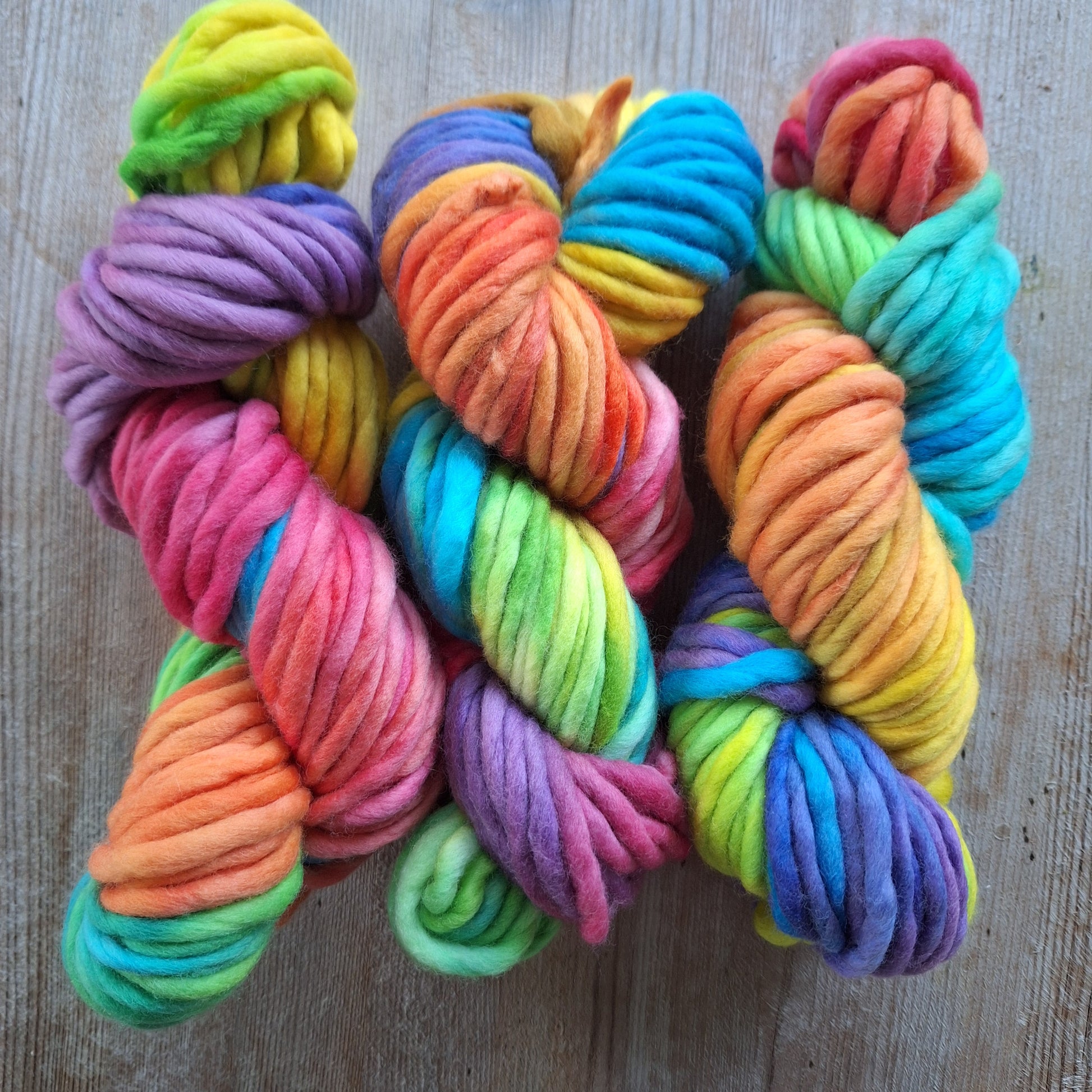 Colorful skeins of rainbow pencil roving yarn on a wooden surface
