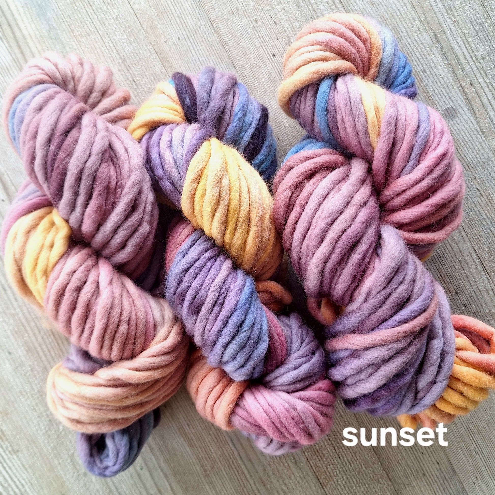 Multicolored yarn skeins on a wooden surface with 'sunset' text.