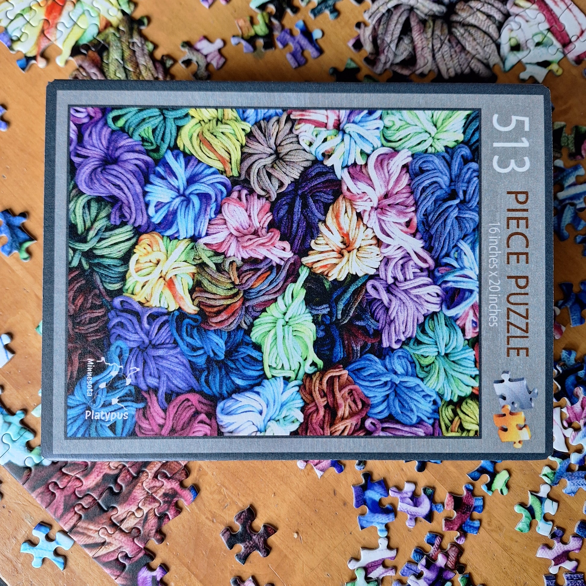 Puzzle box with colorful potholder loops design and scattered puzzle pieces on a wooden surface