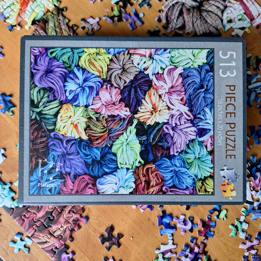 Puzzle box with colorful potholder loops design and scattered puzzle pieces on a wooden surface