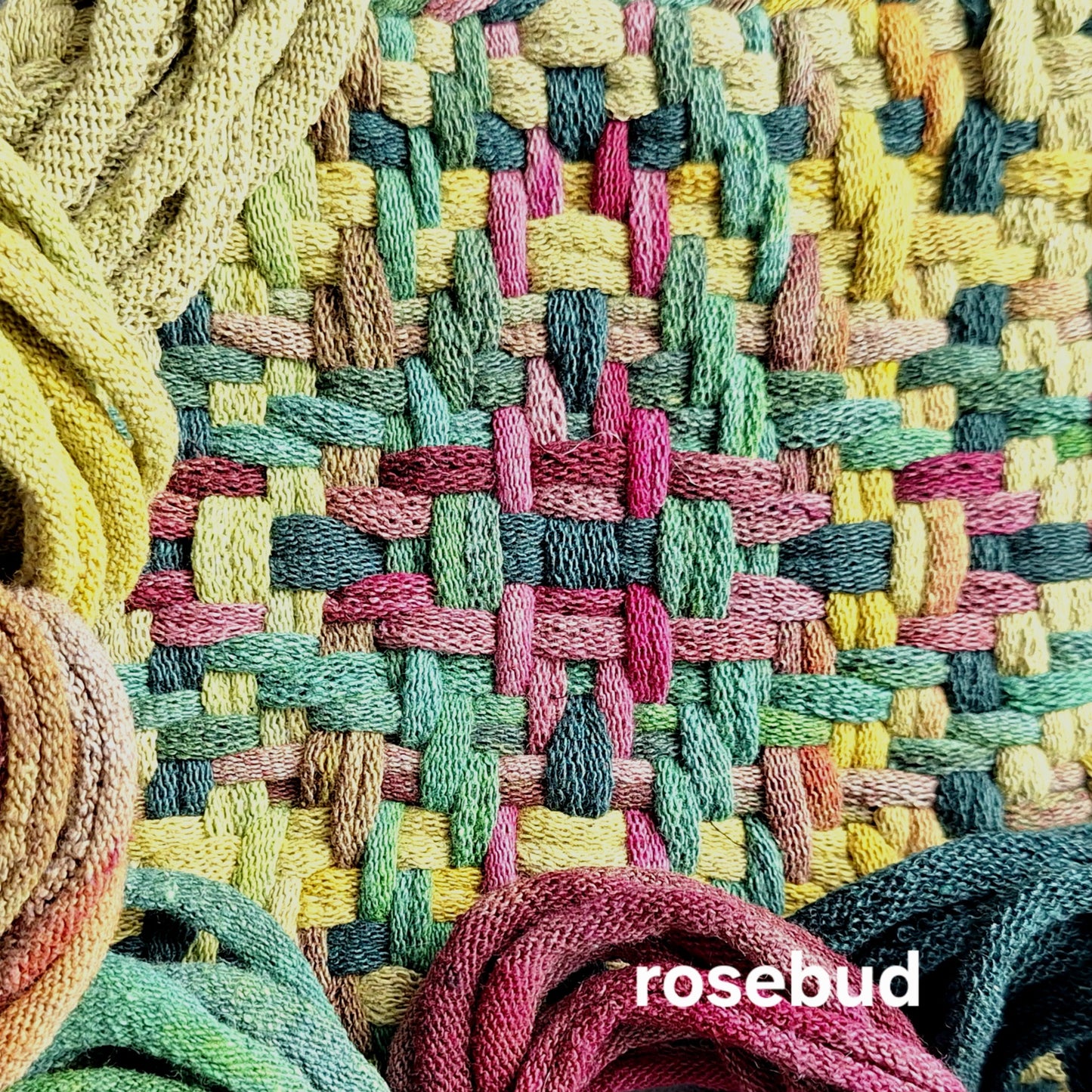 Colorful woven potholder with loop bundles on a woven background, featuring the label 'rosebud'.