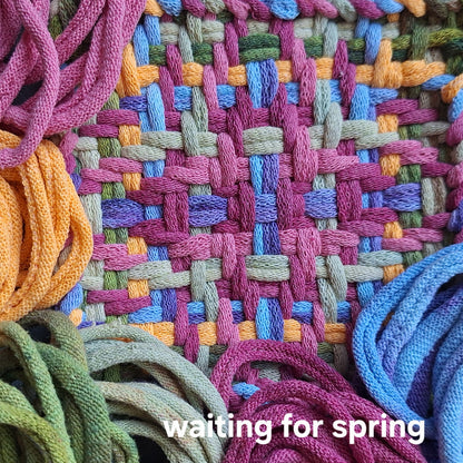 Colorful woven potholder with loop bundles, featuring the text 'waiting for spring'.